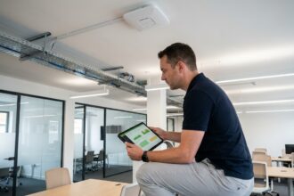Technicien informatique inspectant une borne Wi-Fi 6E montée au plafond dans un bureau d'entreprise moderne avec une tablette affichant un tableau de bord réseau